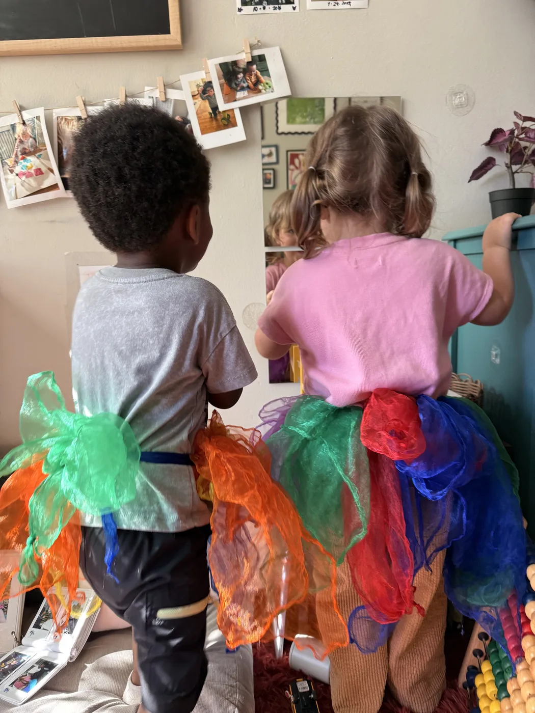 Two toddlers in colorful tulle skirts at the wall of family photos