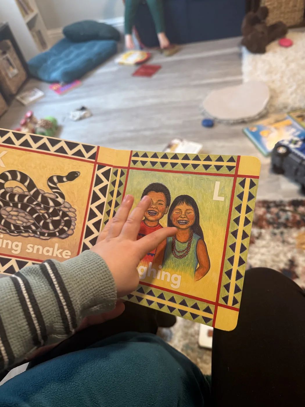 An adult hand pointing at an illustrated alphabet book with children of different backgrounds