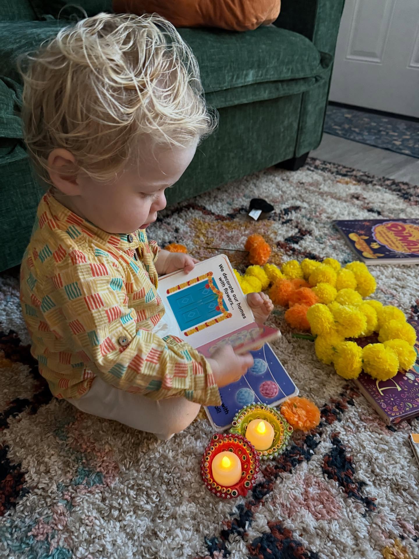 A toddler reading a picture book by candlelight surrounded by marigold garlands