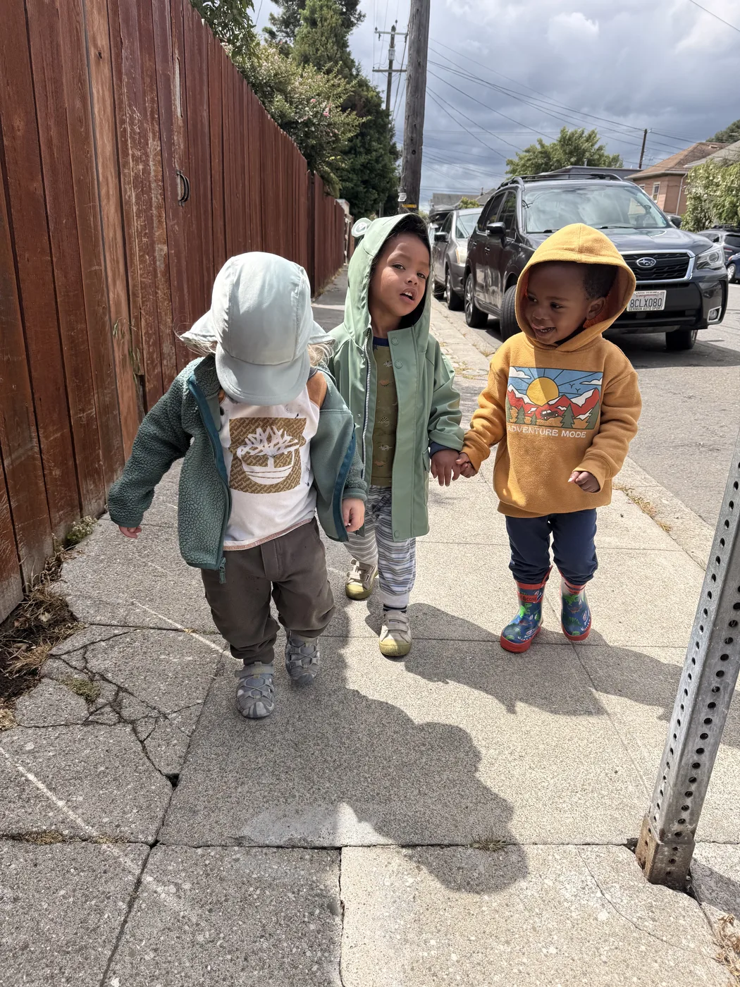 Three toddlers walking hand in hand down a Berkeley sidewalk