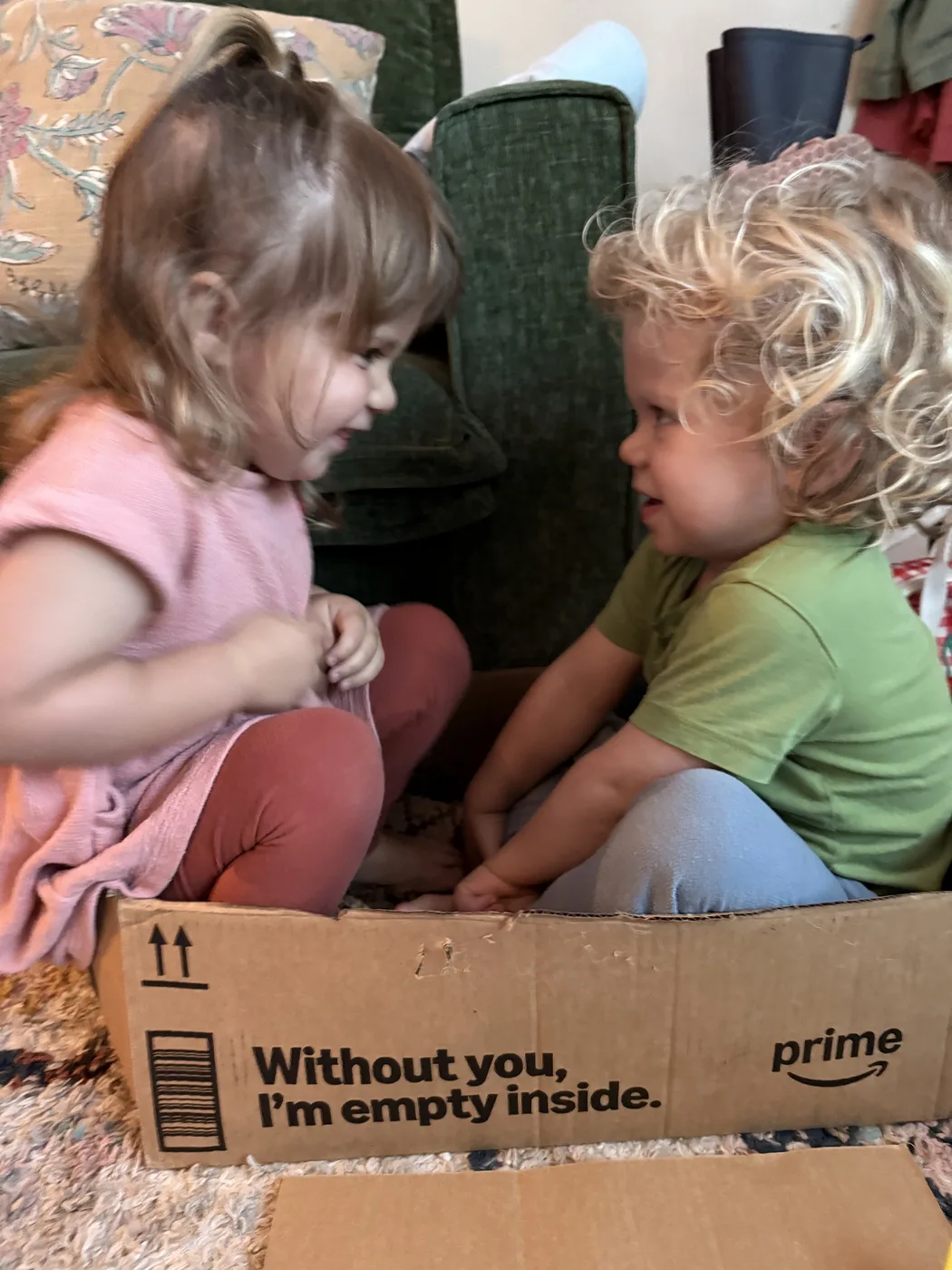 Two toddlers sitting face to face over a cardboard box, talking