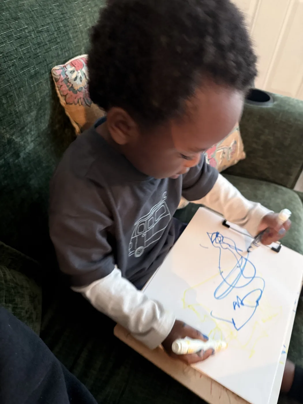 A toddler drawing loops with a marker on paper clipped to a board