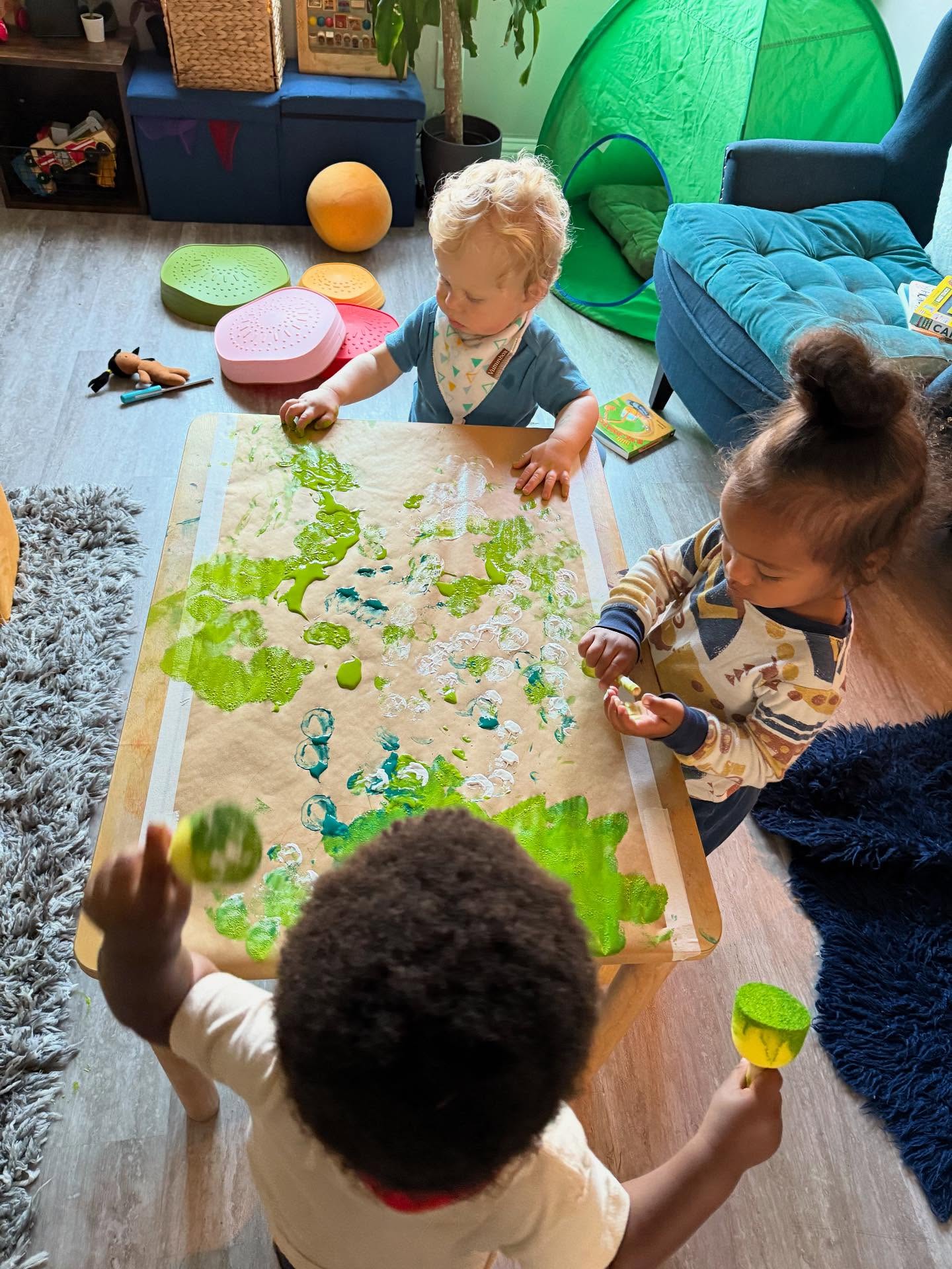 Toddlers sponge-painting together at a table covered in brown paper