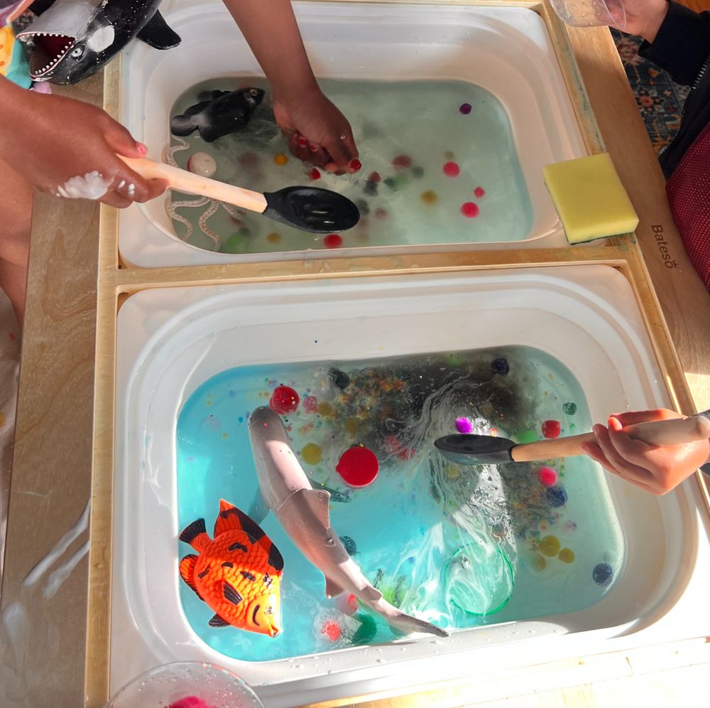 Toddlers scooping toy fish and beads in water bins