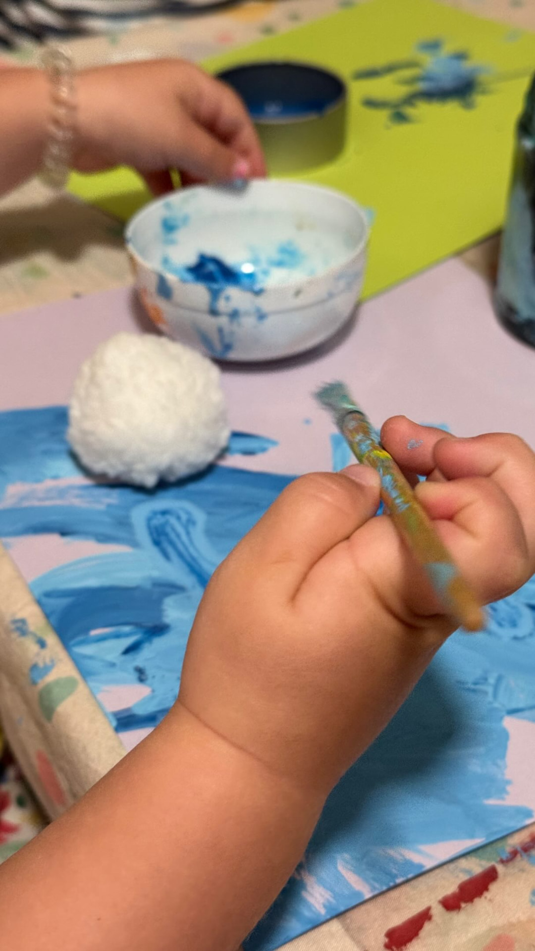A small child's hand holding a paintbrush with blue paint