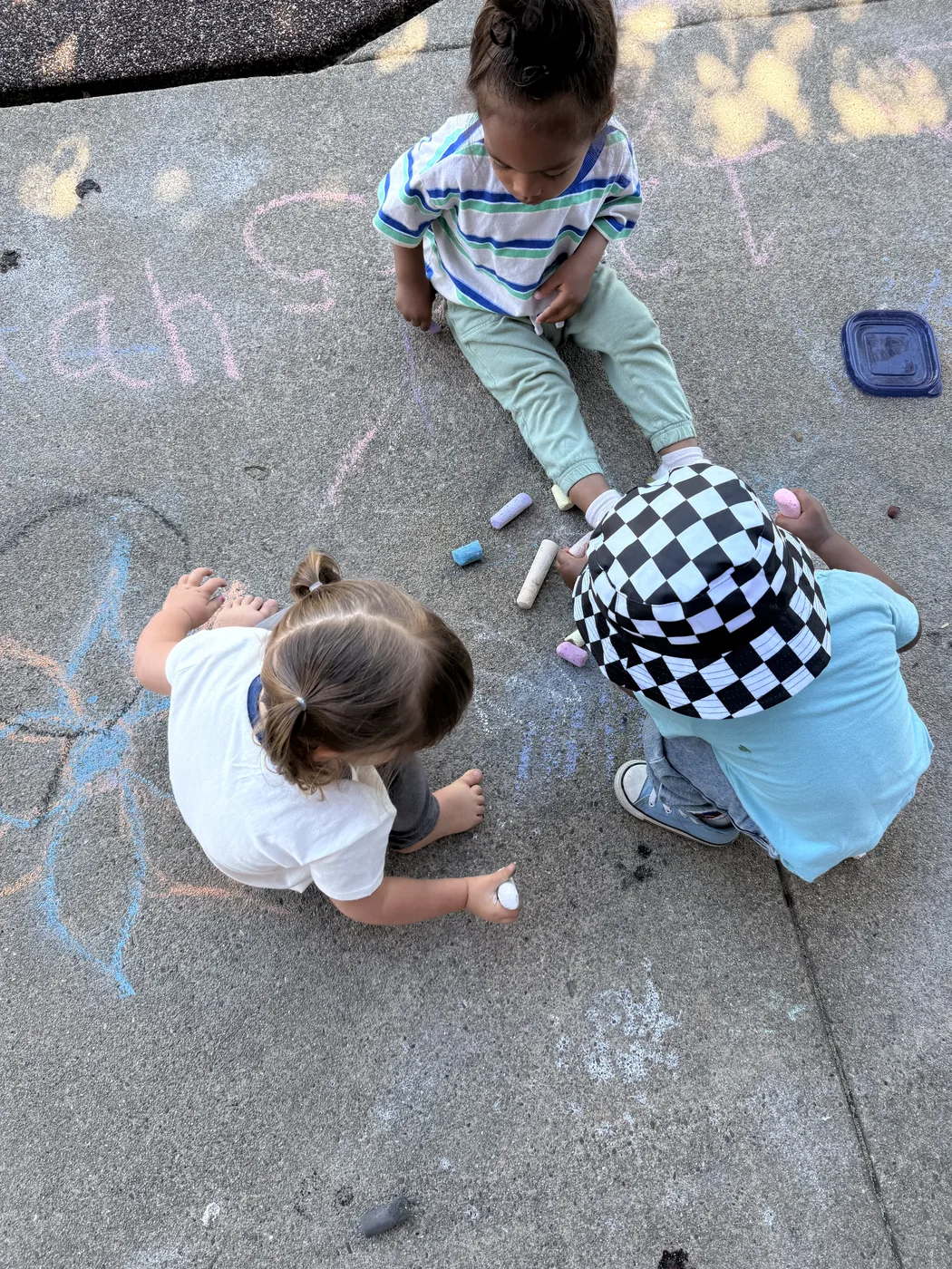 Three children drawing with chalk on the sidewalk