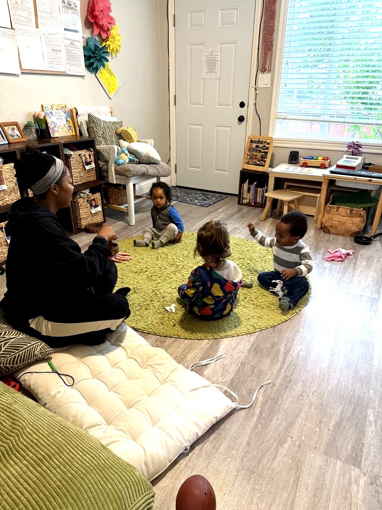 Jo sitting on the rug with three toddlers during morning circle at Little Joey's