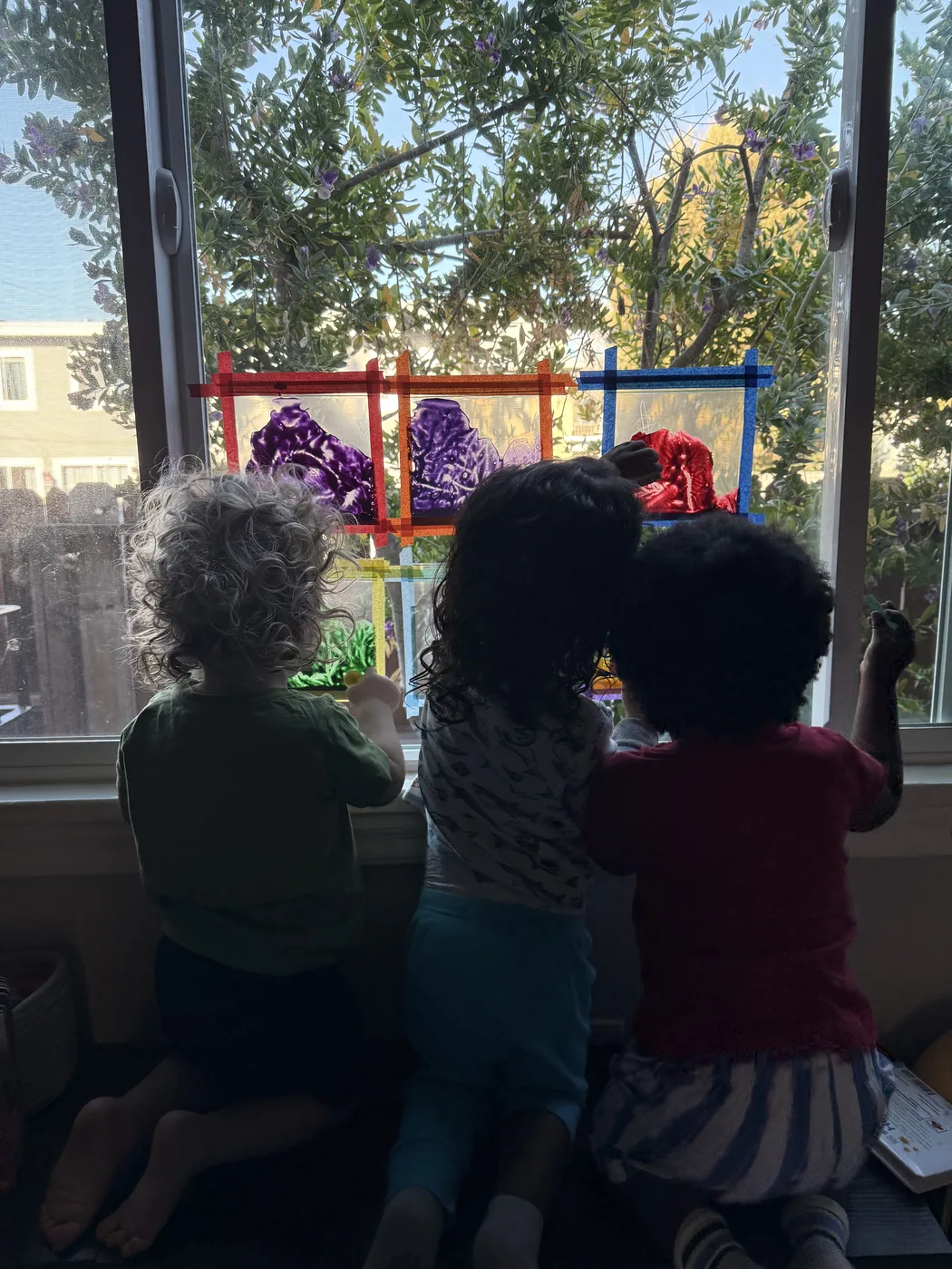 Three children kneeling at a window looking out at the trees