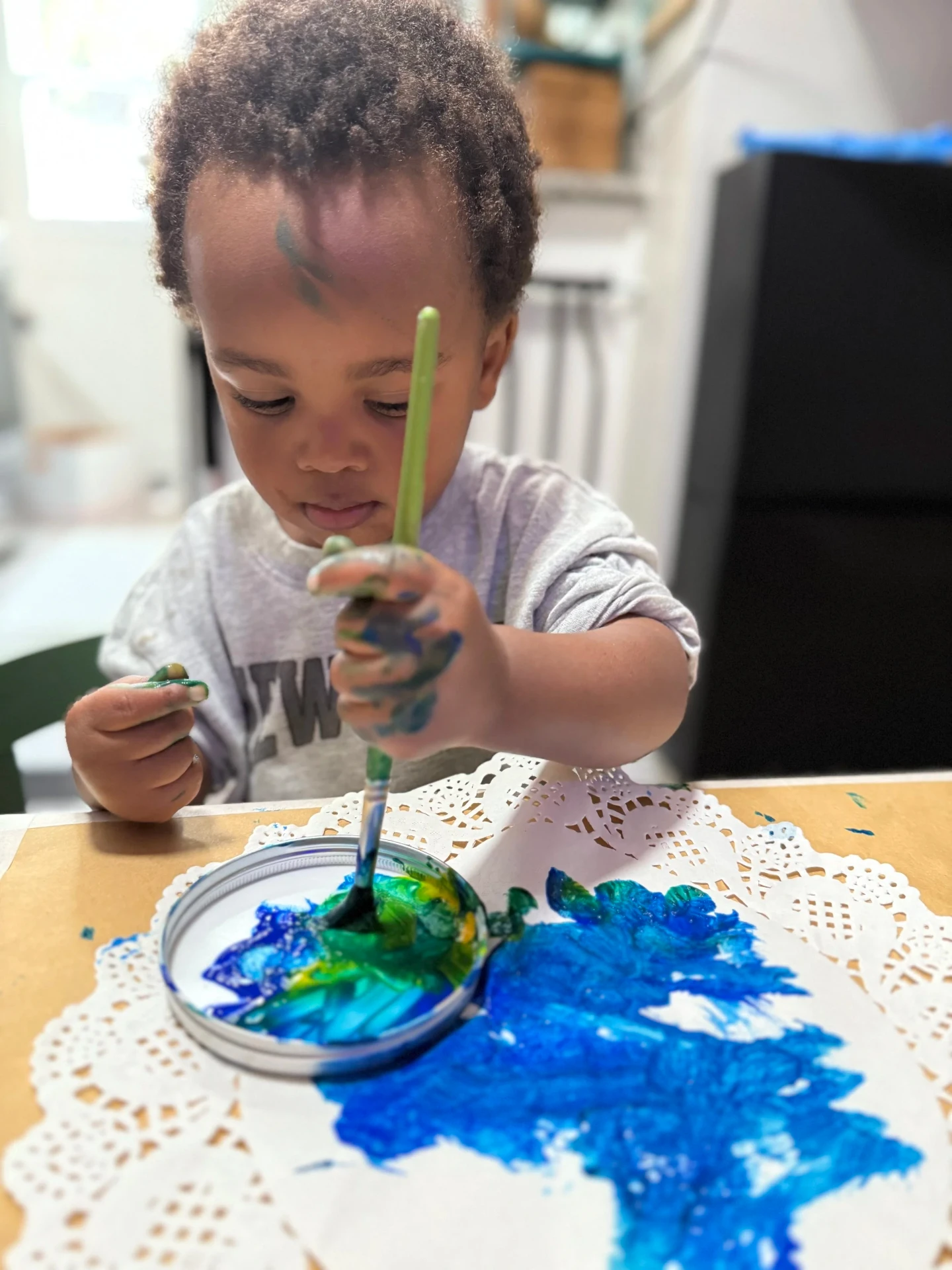 A toddler focused on painting with blue and green colors